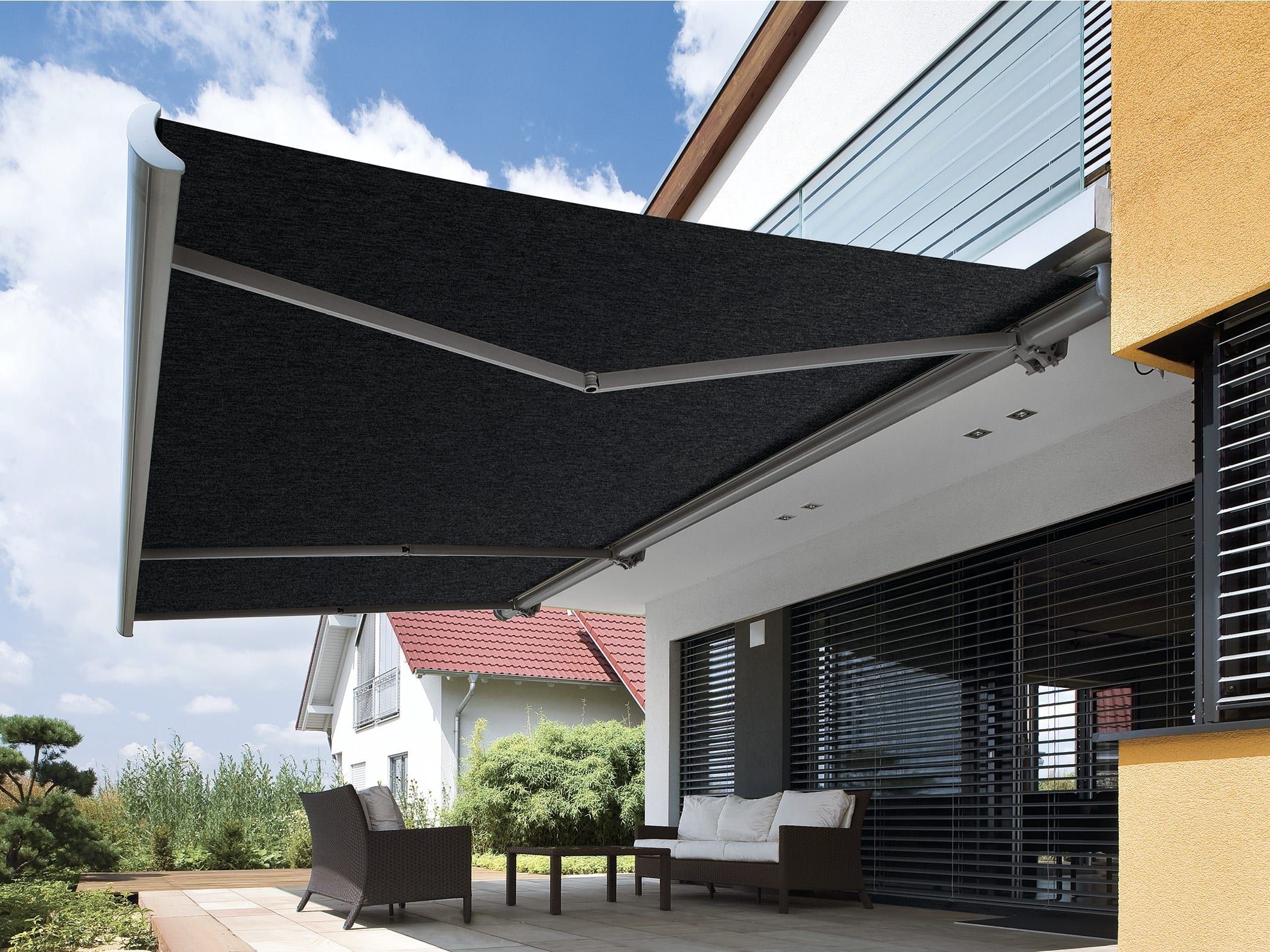 Gelenkarmmarkise über der Terrasse — anthrazitfarbenes Tuch ausgefahren über der Loungeecke am Haus