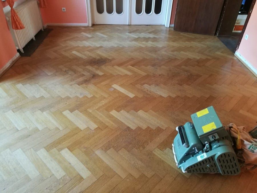Historisches Eichenparkett neu versiegelt — Schleifmaschine auf der halb abgezogenen Fläche