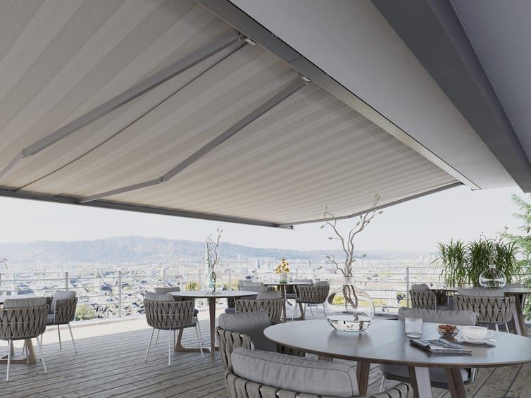 Gelenkarmmarkise über der Terrasse — Blick von unten auf das helle Tuch, Stadt und Tal dahinter