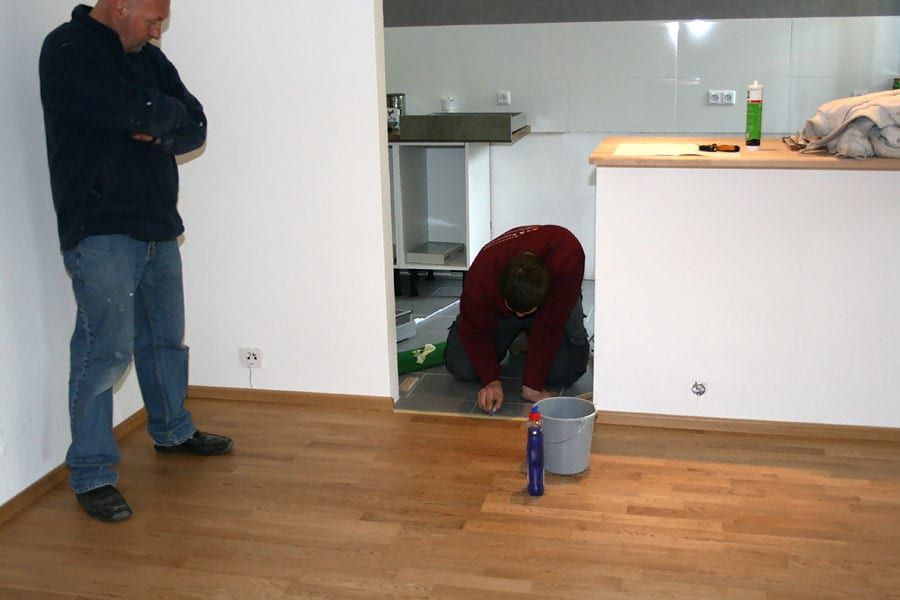 Wohnungsrenovierung mit Fertigparkett Eiche — Handwerker an der Schwelle zum gefliesten Küchenbereich