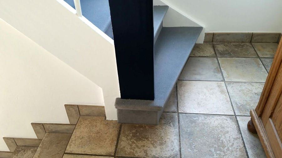 Holztreppe mit hochwertigem Textilbelag — die Wangenseite am Übergang zum Fliesenboden