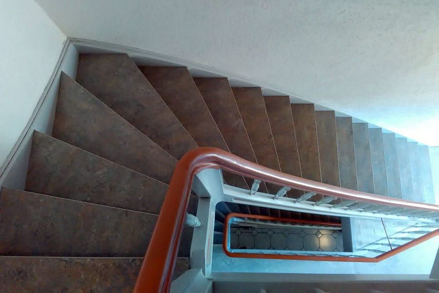 Treppenhausstufen mit Linoleum — Blick vom Podest über den Handlauf in das Treppenauge