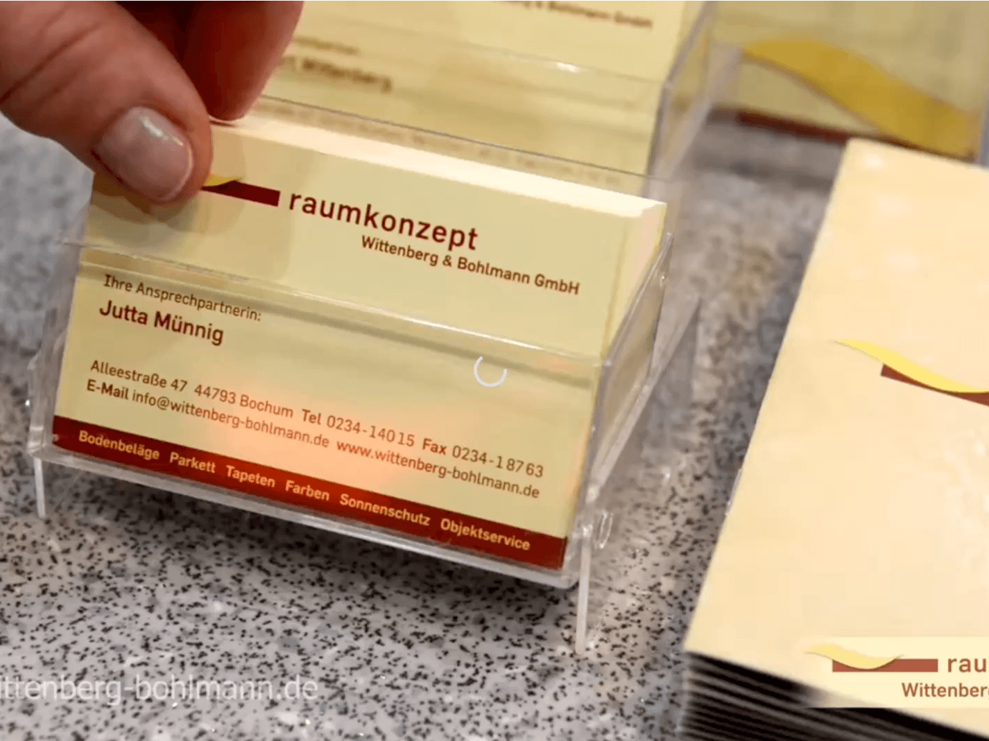 Hand entnimmt eine Visitenkarte von Raumkonzept aus einem Kartenhalter